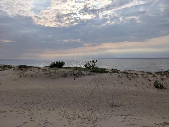 Sand dunes in the foreground, beautiful sun beams and clouds over the lake