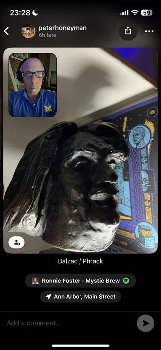This appears to be a social media post showing what looks like a bronze or dark metal sculpture of a face in profile. The sculpture has classical features and appears to be mounted or displayed, with some colorful decorative elements visible in the background that have blue and gold coloring.

There’s a video call overlay in the top-left corner showing someone in a blue shirt (appears to be a Michigan “M” logo), and the post is labeled “Balzac / Phrack” at the bottom. The location shows “Ann Ar…