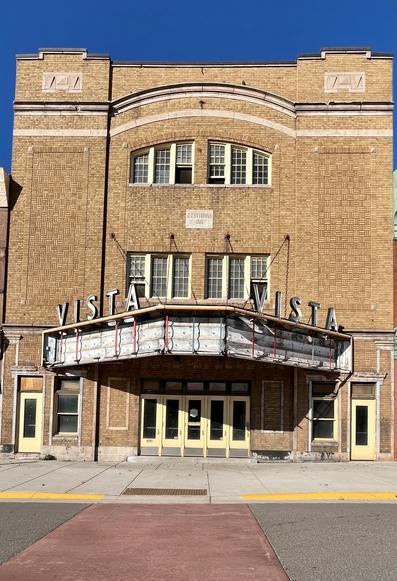 The photo shows the Vista Theater in Negaunee, Michigan. The theater, constructed in 1925, is a three-story building made of yellow-buff brick. It was listed on the National Register of Historic Places in 2005. The building was condemned in 2020 after a roof collapse, but restoration efforts have been underway since then. 