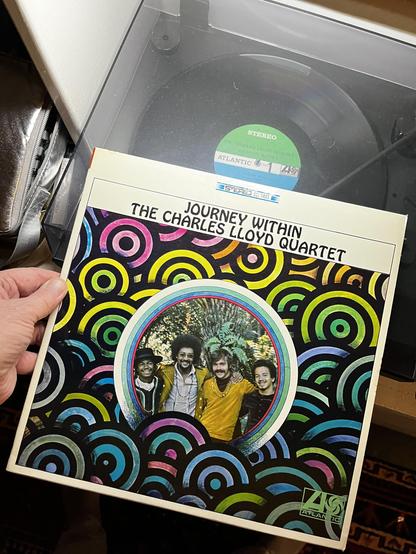 I am holding a vinyl record album cover for "The Journey Within" by the Charles Lloyd Quartet. The album is on Atlantic Records (catalog number 1459) and is labeled as stereo.

The album cover features vibrant, psychedelic artwork typical of the late 1960s era, with colorful concentric circles in pink, yellow, green, blue, and other bright colors creating a swirling pattern across a black background. In the center is a circular photograph of the quartet members - four musicians smiling at the c…