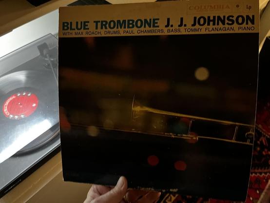This photo shows a classic jazz album from the legendary trombonist J.J. Johnson.

The Album:
"Blue Trombone" by J.J. Johnson

Released on Columbia Records

Features an all-star lineup: Max Roach (drums), Paul Chambers (bass), Tommy Flanagan (piano)

Album Design:
Golden/tan header with bold black text

Atmospheric cover photo showing Johnson's trombone in dramatic lighting against a dark background

The brass trombone gleams in warm tones

Moody, artistic photography typical of late 1950s jazz…