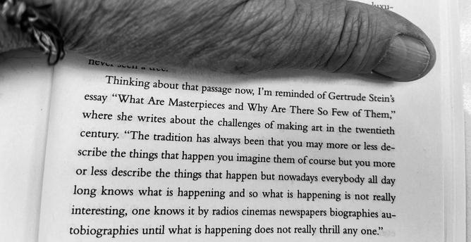 A black-and-white close-up of my thumb pressing down the top corner of a book page to keep it open, the wrinkled skin and nail taking up the top portion of the frame in sharp, heavily-textured detail. Below it, the page shows a paragraph where the author reflects on a Gertrude Stein essay — "What Are Masterpieces and Why Are There So Few of Them" — about the difficulty of making art in an era of constant media saturation, where the sheer volume of things "everybody all day long knows" through r…
