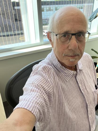 It’s me! In the emeritus office! In a brand new Herman Miller chair!

A close-up selfie of an older man [hmph] sitting in a black mesh-back office chair (Herman Miller style) in the same emeritus office as the previous photo. He's balding [ok ok enough] with white hair [oh ok so I am old already!] on the sides, wears rectangular black-framed glasses, and has a white mustache and soul patch. He's wearing a lavender-and-white striped button-down shirt, open at the collar, with a small beaded neck…